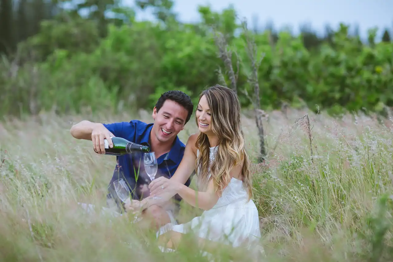 Couple pouring Lokelani sparkling rosé in a grassy field
