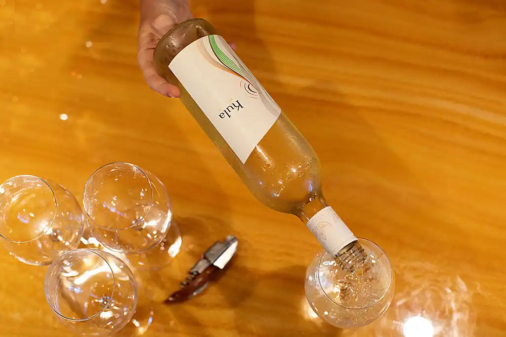 Pouring Kula white wine into glasses on a wooden table