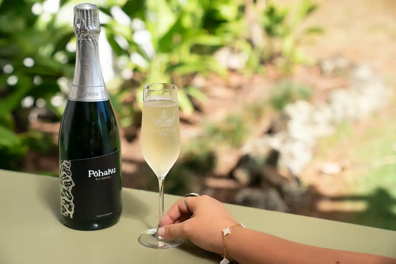 Bottle and glass of Pōhaku sparkling wine on a garden table