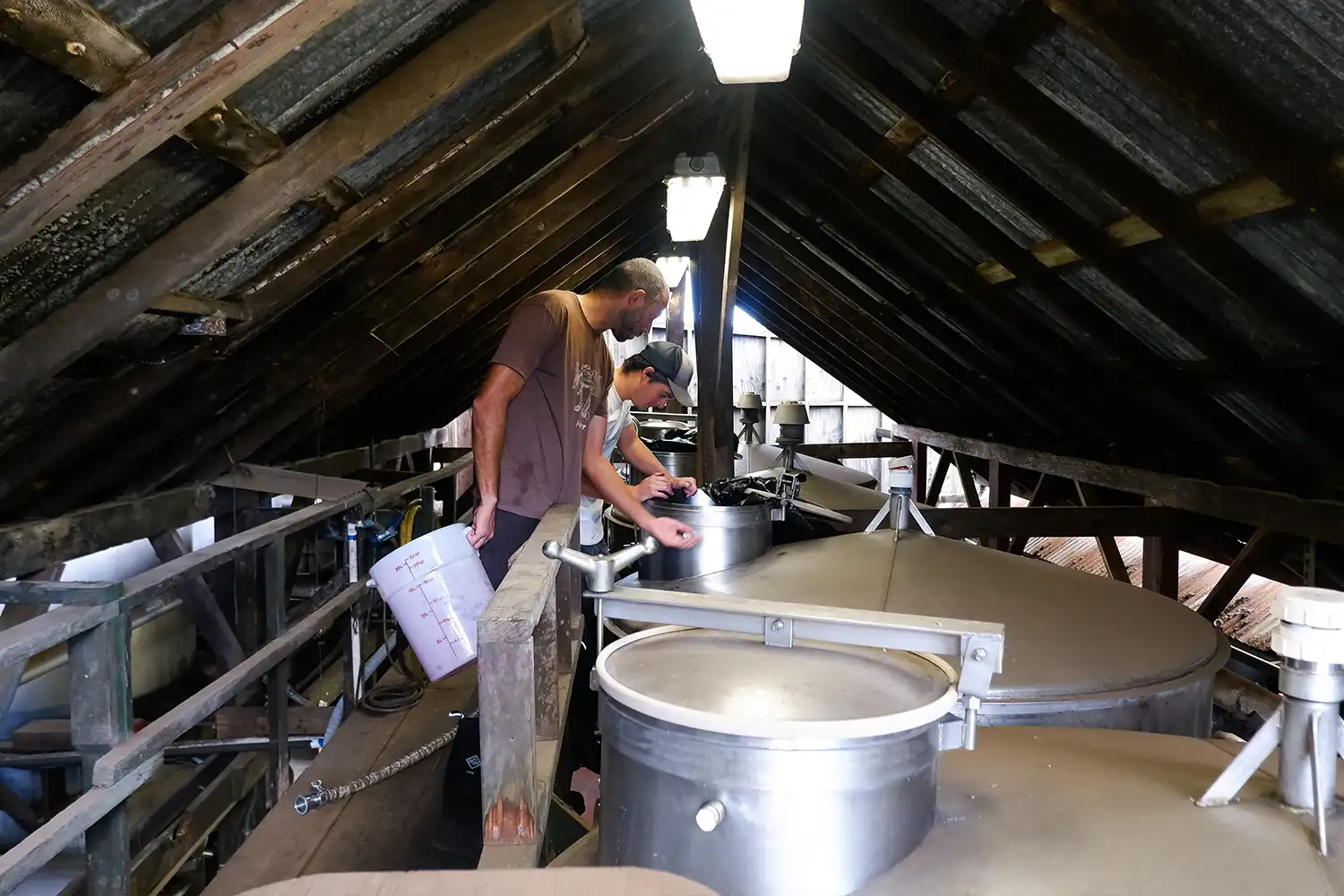 Winemaker working at stainless steel tanks under the winery's wooden roof